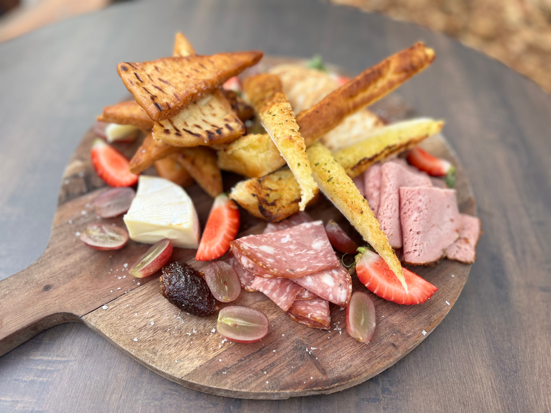 A generous share platter with sliced meats, cheeses, garlic bread, crackers and fresh fruit